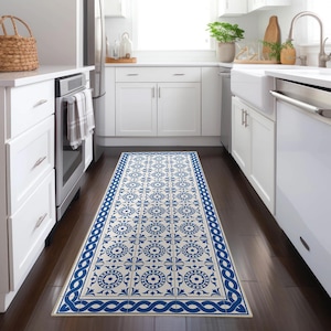 Puede incluir: Una alfombra rectangular para pasillo de cocina con un patrón de baldosas azul y blanco repetido. El diseño presenta motivos circulares y florales dentro de cada baldosa, enmarcados por un borde azul con un patrón ondulado. La alfombra está colocada sobre un suelo de madera oscura.