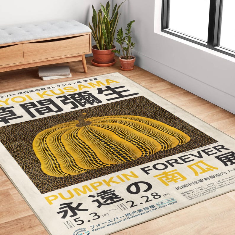 Op de afbeelding: Een rechthoekig vloerkleed met een geel pompoenontwerp met zwarte stippen. Het vloerkleed heeft Japanse tekst en de woorden "PUMPKIN FOREVER" in geel en zwart. Het vloerkleed ligt op een houten vloer.