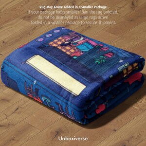 May include: Folded blue rug with a colorful illustration of a building and other elements. The rug has a white rectangular design and the text "Unboxiverse" is visible. The text "Rug May Arrive Folded in a Smaller Package" is also visible.