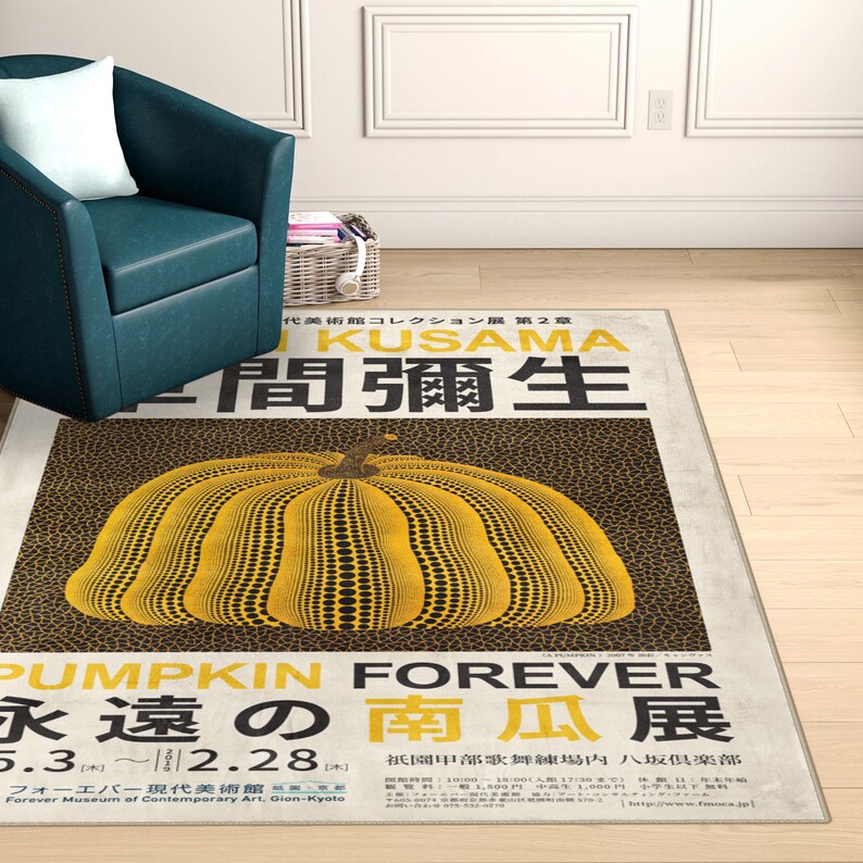 Op de afbeelding: Een rechthoekig vloerkleed met een groot geel pompoenontwerp met zwarte stippen op een bruine gespikkelde achtergrond. Het vloerkleed heeft Japanse tekst en de woorden "PUMPKIN FOREVER" in het geel. Het vloerkleed ligt op een lichtgekleurde vloer.
