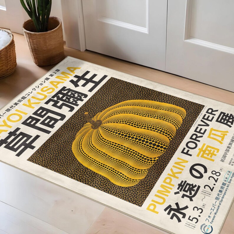 Op de afbeelding: Een rechthoekige deurmat met een grote gele pompoen met zwarte stippenpatronen. De mat heeft Japanse tekst en de woorden "PUMPKIN FOREVER" in het geel. De achtergrond is donkerbruin met een cr&egrave;mekleurige rand.