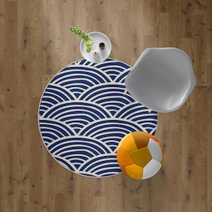 Pode incluir: Vista aérea de um tapete redondo com um padrão de ondas azuis e brancas, uma cadeira cinza, uma bola decorativa com painéis amarelos, laranja e branco, e uma pequena mesa branca com uma planta e um vaso em um piso de madeira.
