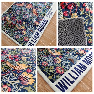 Op de afbeelding: Een rechthoekig tapijt met een gedetailleerd bloemen- en vogelpatroon in tinten blauw, groen, geel en rood. Het tapijt heeft de tekst "WILLIAM MORRIS" in wit op een blauwe achtergrond. Het ontwerp bevat aardbeien en andere botanische elementen.