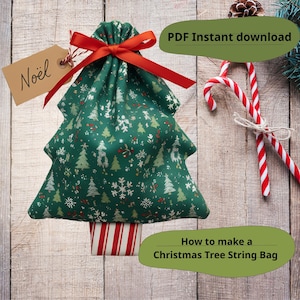 Könnte beinhalten: Ein grüner Weihnachtsbaum-förmiger Kordelzugbeutel mit rotem Band, gefüllt mit einem Geschenk. Der Beutel ist mit weißen und grünen Weihnachtsbäumen und Schneeflocken verziert. Ein Anhänger mit der Aufschrift "Noël" hängt am Beutel.