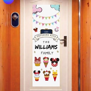 May include: A white door decoration with a banner that says "Cruising with The Williams Family." The design includes cartoon images of desserts and Mickey Mouse ears. The door number is 1205. The background is a wooden hallway.