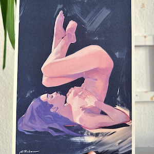 Könnte beinhalten: Ein Kunstdruck mit einer liegenden Figur, dargestellt in sanften Rosa- und Lilatönen. Das Kunstwerk zeigt eine Person mit lila Haaren vor einem dunklen Hintergrund. Der Druck wird von einer Hand mit Tätowierung gehalten.