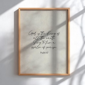 Può includere: Stampa incorniciata con sfondo beige chiaro e cornice in legno. Il testo "God is the King of all the earth. Sing to him a psalm of praise. Psalm 47" è scritto in corsivo nero.