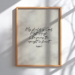 Op de afbeelding: Een ingelijste print met een lichtbeige achtergrond en een houten frame. De print bevat elegante cursieve tekst die luidt: "Mijn schild is God, de Allerhoogste. Die de oprechten van hart redt. Psalm 7."
