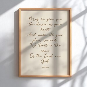 Puede incluir: Una impresión enmarcada con un fondo beige claro y un marco de madera. La impresión presenta un texto elegante, escrito a mano, en color marrón cálido, que incluye las palabras "May he give you the desire of your heart". El texto es del Salmo 20.