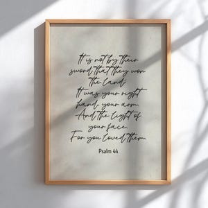 Könnte beinhalten: Ein gerahmter Druck mit hellbeigem Hintergrund und Holzrahmen. Der Druck zeigt schwarzen handgeschriebenen Text aus Psalm 44, einschließlich der Sätze „Es ist nicht durch ihr Schwert“ und „Denn du hast sie geliebt“.