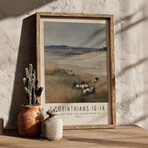 Puede incluir: Un grabado enmarcado que presenta un paisaje pastoral con ovejas pastando en un campo. La obra de arte está en un marco de madera e incluye el texto "1 Corintios 16:14" y "Hágase todo entre vosotros con amor."