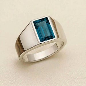 May include: A silver ring with a rectangular, teal-colored gemstone. The ring has a polished, metallic band and a bezel setting that highlights the gemstone. The ring's design is simple yet elegant, suitable for everyday wear.