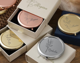 May include: Several personalised compact mirrors in gold, rose gold, and silver. Each mirror features a floral engraving and a name, presented in individual cream-coloured gift boxes with floral detailing. The mirrors are ideal for gifting.