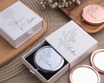 May include: Gift sets featuring white boxes with floral designs and names, and rose gold and silver compact mirrors. The items are displayed on a wooden surface, ideal for personalized gifting.