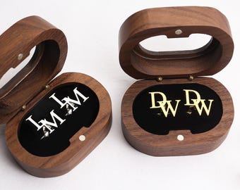 May include: Two wooden jewellery boxes with open lids, revealing black interiors and initialled jewellery. One box has silver initials "I M", the other has gold initials "D W". Two pairs of gold initialled earrings are also visible.