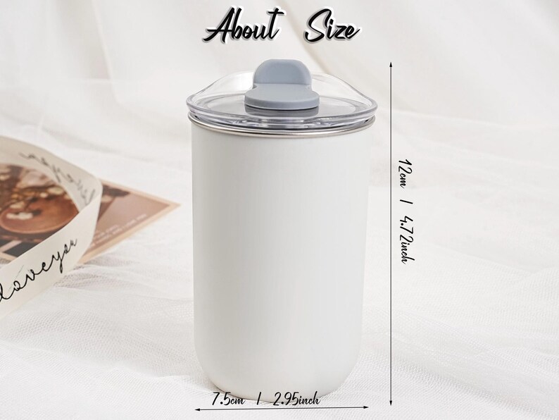 Op de afbeelding: Een witte beker met een doorzichtig deksel en een grijze klapsluiting. De beker is 12 cm hoog en 7,5 cm breed. De tekst "About Size" staat bovenaan de afbeelding.