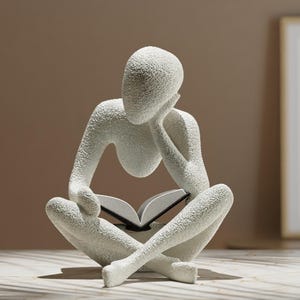 May include: A white, textured sculpture of a person reading a book while sitting cross-legged. The figure is in a thoughtful pose, with their head resting on their hand. This decorative sculpture is suitable for home decor.