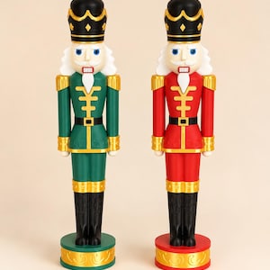 May include: Two nutcracker figures standing side by side. One figure wears a green uniform with gold trim, and the other wears a red uniform with gold trim. Both have black hats, white hair, and black boots, standing on circular bases.