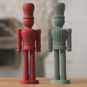 May include: Two standing nutcracker figurines. The left figure is solid red with a textured, matte surface. The right figure is sage green and features a distinct vertical ribbed or slatted design throughout its entire body, hat, and limbs.