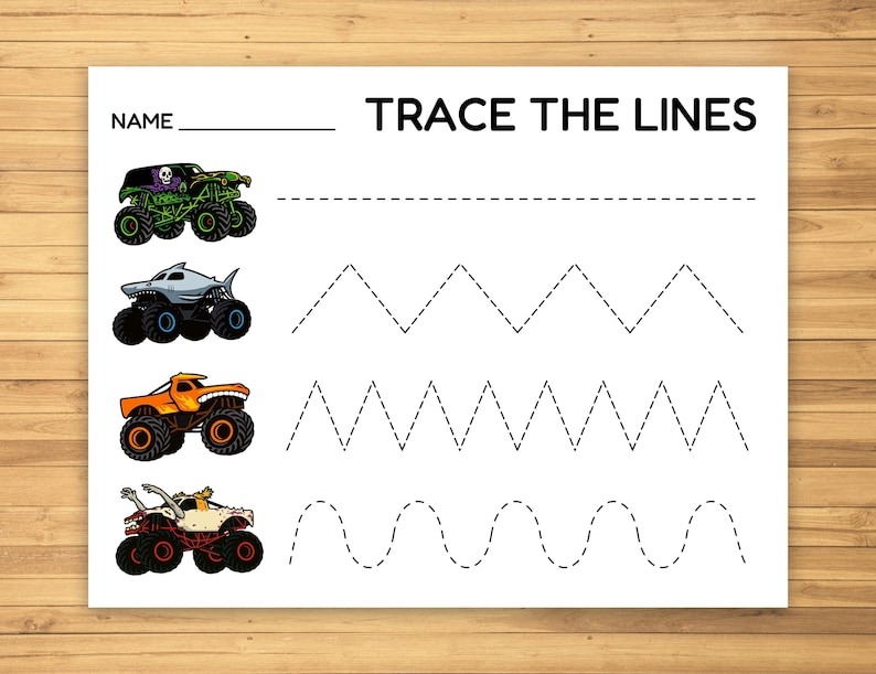 May include: White paper with the text "TRACE THE LINES" and a space for a name. Features illustrations of monster trucks and dotted lines for tracing practice. Includes a green, shark, orange, and white monster truck.