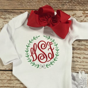 Pode incluir: Batista branca para beb&eacute; com mangas compridas e uma bainha com babados. A bata tem um monograma vermelho com as letras "SSF" dentro de uma coroa verde.