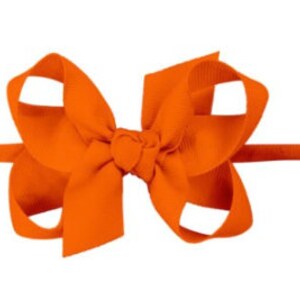 May include: Orange fabric headband with a large bow. The bow is made of a soft, textured fabric and is tied in a simple knot.