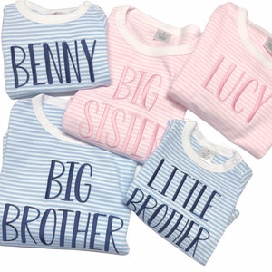 Puede incluir: Cuatro bodies de beb&eacute; a rayas con texto bordado. Dos bodies azules dicen "Hermano Mayor" y "Hermano Menor". Dos bodies rosas dicen "Hermana Mayor" y "Lucy". Un body azul dice "Benny".