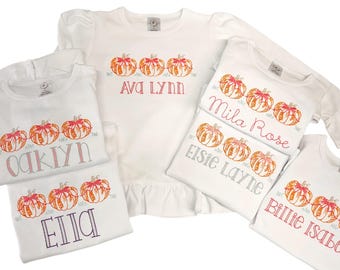 Könnte beinhalten: Fünf weiße T-Shirts mit gestickten Kürbissen und Namen. Die Namen sind Ava Lynn, Oaklyn, Ella, Elsie Layne und Billie Isabelle.