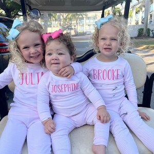 Puede incluir: Tres ni&ntilde;as peque&ntilde;as con pijamas de rayas blancas y rosas con sus nombres, "Julia", "Josephine" y "Brooke", bordados en la parte delantera. Las ni&ntilde;as est&aacute;n sentadas en un carrito de golf.