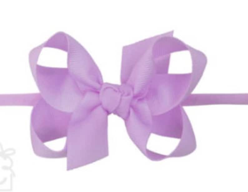 May include: A light purple hair bow with a simple design. The bow is made of a soft, silky fabric and is tied with a knot in the center.