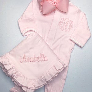May include: Pink baby outfit with a matching blanket. The outfit has a white trim and is embroidered with the letters "A.A.R." The blanket has a ruffled edge and is embroidered with the name "Arabella".
