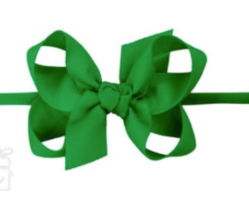 May include: A green hair bow with a simple, classic design. The bow is made of a soft, smooth fabric and is attached to a stretchy headband.