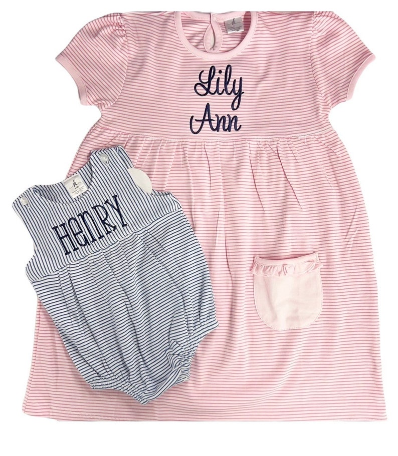 May include: Pink and white striped dress with the name "Lily Ann" embroidered in navy blue. A matching blue and white striped romper with the name "Henry" is also included. Both items are children's clothing.