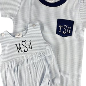 May include: Two-piece baby outfit set. The set includes a light blue and white striped t-shirt with a navy blue pocket and trim, and a matching romper. Both pieces feature embroidered initials. The romper has a bubble silhouette.