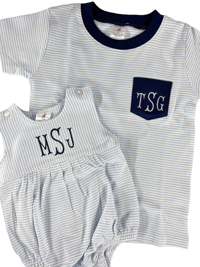 May include: Two-piece baby outfit set. The set includes a light blue and white striped t-shirt with a navy blue pocket and trim, and a matching romper. Both pieces feature embroidered initials. The romper has a bubble silhouette.