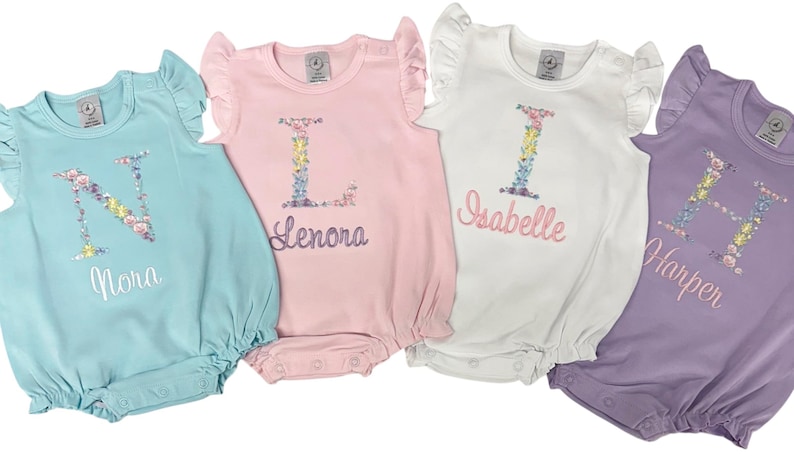 May include: Four baby rompers in pastel colors: light blue, pink, white, and lavender. Each romper features a floral initial and name embroidery. The rompers have ruffled sleeves and a bubble bottom.