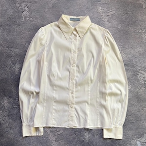 Pode incluir: Camisa creme com botões, mangas compridas e gola clássica. A camisa apresenta um corte sob medida com costuras verticais e mangas bufantes sutis. A etiqueta Prada é visível na gola.