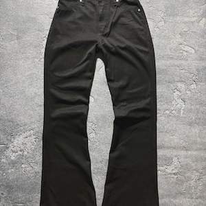 Puede incluir: Pantalones vaqueros negros con diseño de pernera acampanada. Los pantalones tienen un estilo clásico de cinco bolsillos, cierre de botón y cremallera, y una etiqueta roja en la parte trasera. La tela parece resistente.