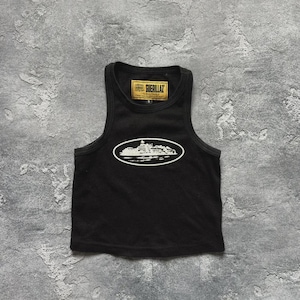 Może przedstawiać: Czarny, prążkowany top na ramiączkach z białym owalnym nadrukiem. Grafika przedstawia stylizowany obraz budynku. Top ma małą prostokątną metkę z napisem "GUERILLAZ".