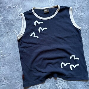 Puede incluir: Camiseta sin mangas azul marino con ribete blanco y un gr&aacute;fico de p&aacute;jaros blancos. La camiseta tiene la etiqueta de la marca "Evisu". La camiseta est&aacute; hecha de un material suave.