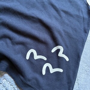 Puede incluir: Camiseta azul marino con tres dise&ntilde;os blancos en forma de ola. La camiseta tiene un dise&ntilde;o simple y minimalista, con los gr&aacute;ficos de olas cerca del borde inferior. La tela parece suave y c&oacute;moda.