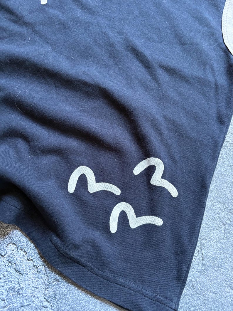 Puede incluir: Camiseta azul marino con tres dise&ntilde;os blancos en forma de ola. La camiseta tiene un dise&ntilde;o simple y minimalista, con los gr&aacute;ficos de olas cerca del borde inferior. La tela parece suave y c&oacute;moda.