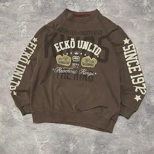 May include: A brown sweatshirt with the text "ECKO UNLTD" in white and gold. The sleeves have the text "ECKO UNLTD" and "SINCE 1972". The sweatshirt has a crew neck and a graphic design on the front.
