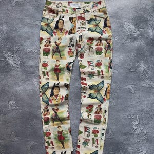 May include: Cream-colored pants featuring a multi-colored collage print of butterflies, various national flags, floral elements, and vintage-style illustrations of people in traditional attire, with a Christian Dior label at the waistband.