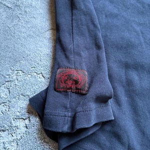 Puede incluir: Camiseta de manga larga azul marino con un parche rojo en la manga. El parche presenta un dise&ntilde;o con detalles rojos y negros. La camiseta est&aacute; hecha de un material suave y c&oacute;modo.
