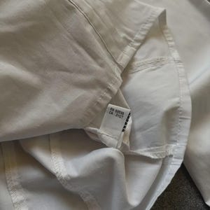 May include: Close-up of a white button-down shirt. The shirt is made of a smooth, crisp fabric. The tag reads RN 68596 CA 31127.