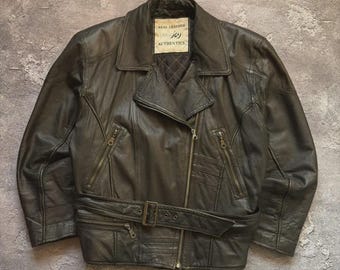 May include: A dark brown leather jacket with a zipper closure and a belt. The jacket has multiple pockets and a collar. The label reads "REAL LEATHER" and "joy AUTHENTICS".