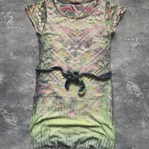 Puede incluir: Vestido de manga corta con un diseño estampado colorido. El vestido presenta un cuello redondo, una cintura ceñida con un lazo y un dobladillo que llega hasta la mitad del muslo. La paleta de colores incluye verde, rosa y amarillo.