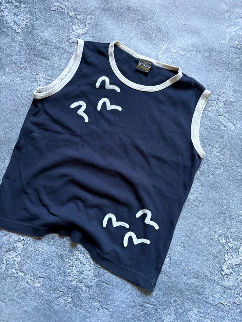 Puede incluir: Top sin mangas azul marino con ribete blanco y gr&aacute;ficos de p&aacute;jaros blancos. El top tiene cuello redondo y una etiqueta que dice "Evisu". La prenda est&aacute; hecha de un material suave.