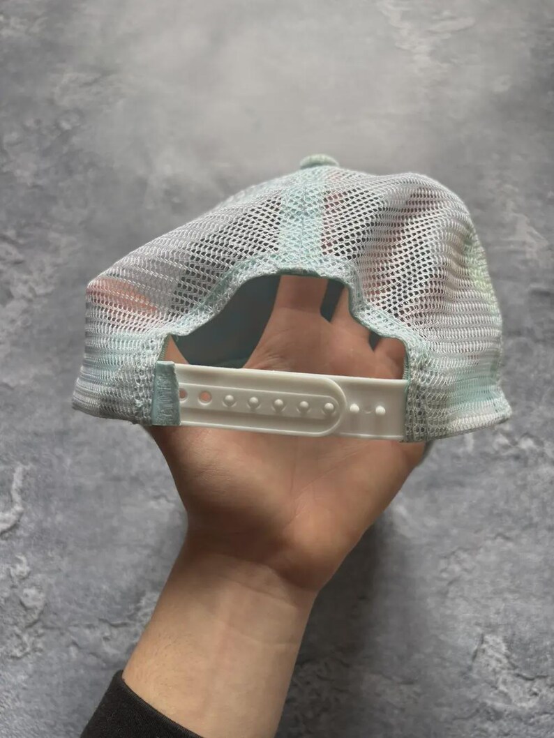 May include: A light blue trucker hat with a white mesh back and a white adjustable strap. The hat has a curved brim and a light blue front panel. The hat is designed to be worn with the brim facing forward.